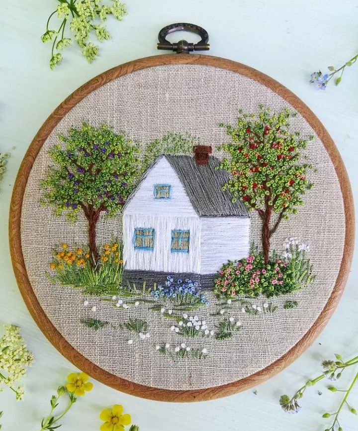 a white house surrounded by trees and flowers on a beige background with an embroidered hoop