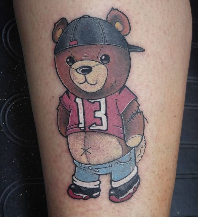 a tattoo with a bear wearing a baseball uniform on it's leg and holding a ball