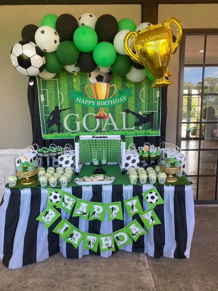 a soccer themed birthday party with green and black decorations, gold foil balloons, white and black striped tablecloths