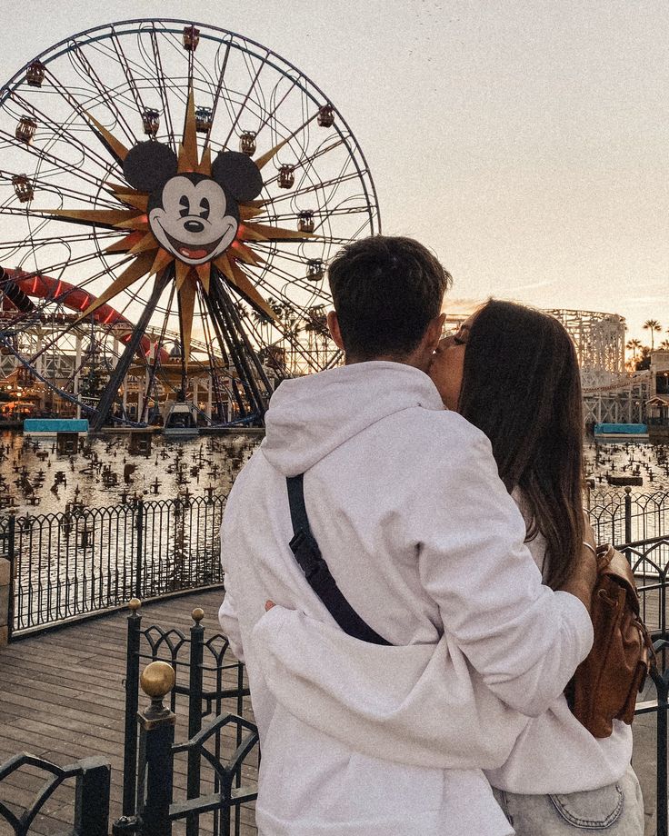 a man and woman kissing in front of a ferris wheel with mickey mouse on it