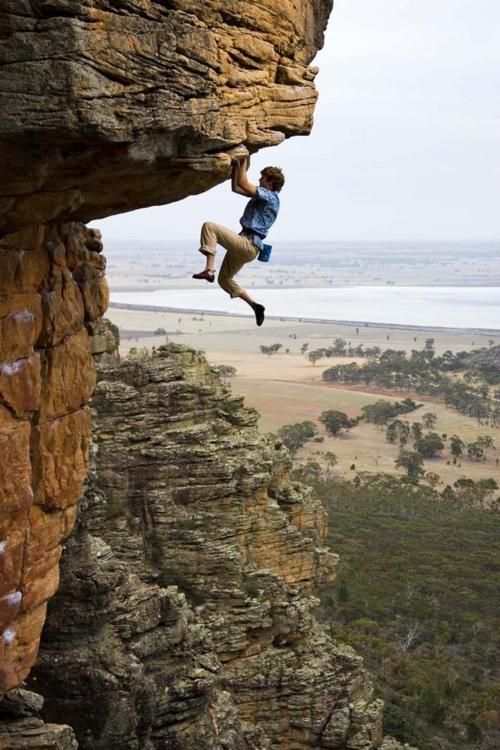 a man climbing up the side of a cliff with his feet in the air while holding onto a rope