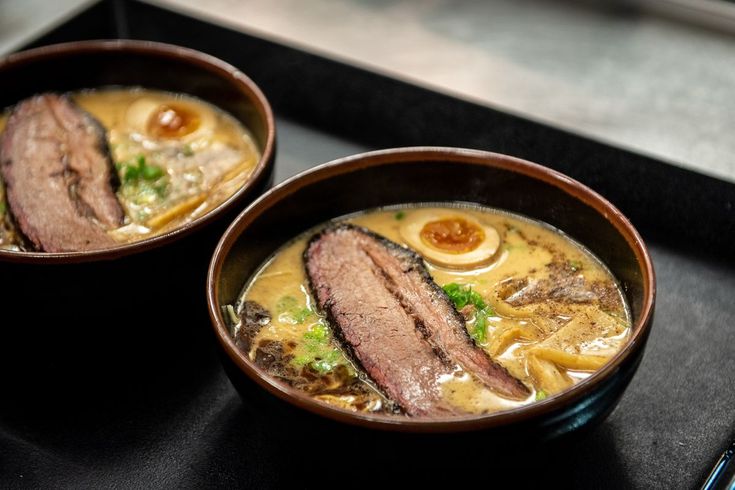 two brown bowls filled with soup on top of a black counter next to chopsticks