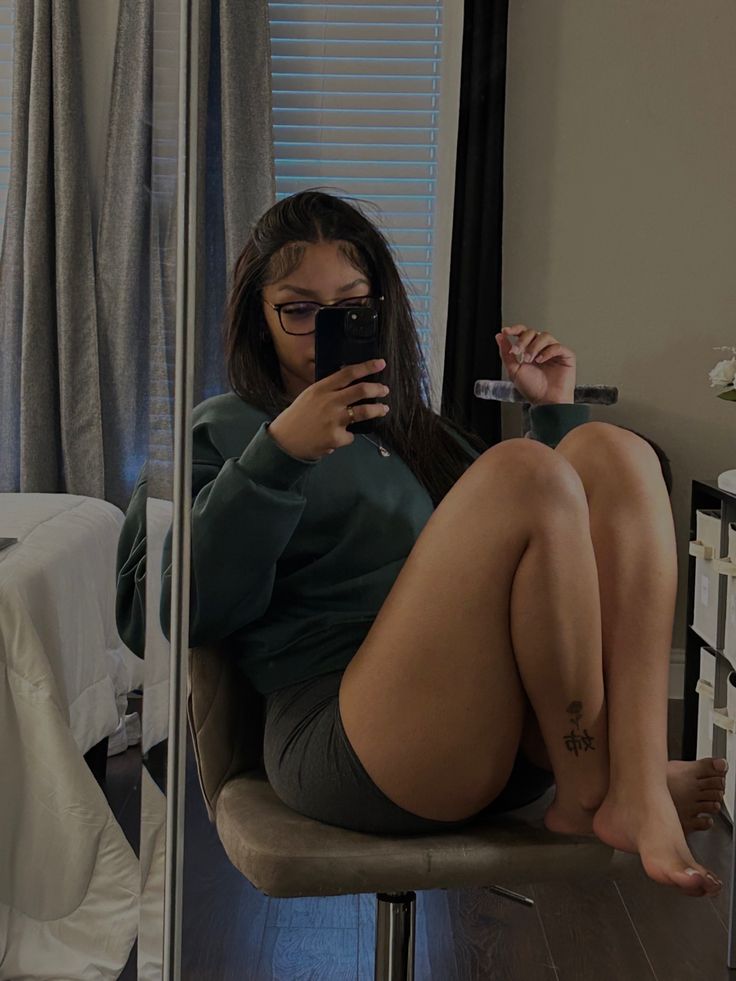 a woman sitting on a chair taking a selfie with her phone in front of the mirror