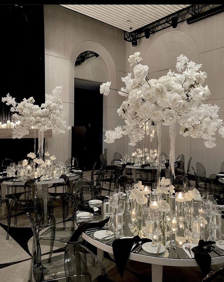 a room filled with tables and chairs covered in white flower centerpieces, surrounded by tall glass vases