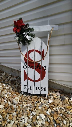 a wooden sign sitting on top of gravel next to a white building with a red santa's sleigh hanging from it