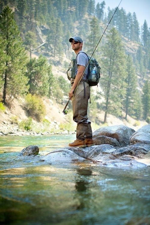 a man standing on top of a rock next to a river holding a fishing pole