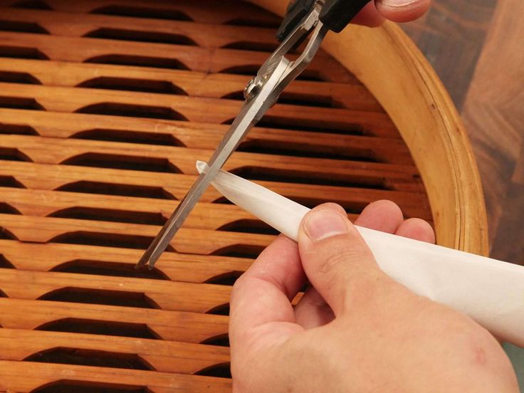 a person cutting paper with scissors on top of a wooden table next to a basket