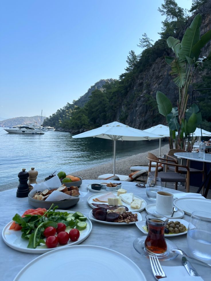 the table is set with food and drinks for two people to enjoy on the beach