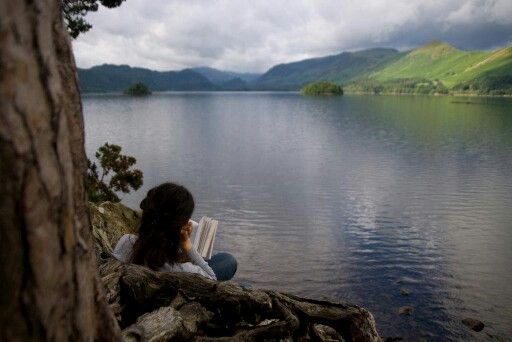 a woman reading a book on the shore of a lake