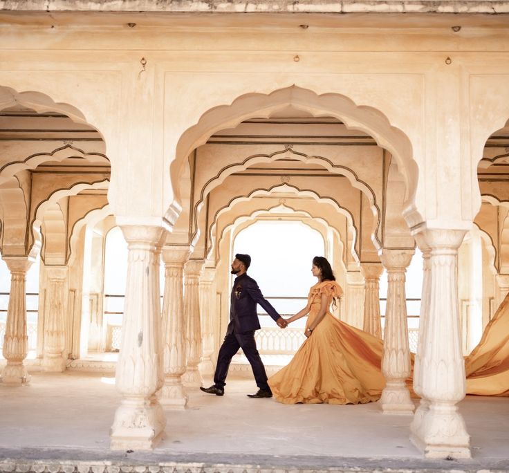 a man and woman holding hands walking through an archway with pillars in front of them