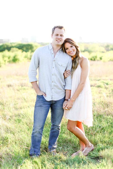 an engaged couple standing in a field with their arms around each other and smiling at the camera