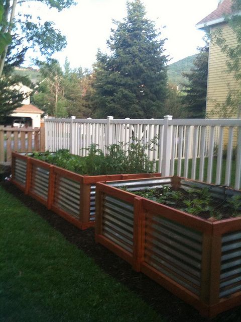 three wooden planters with plants growing in them on the grass next to a fence