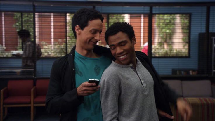 two young men standing next to each other looking at a cell phone in front of them