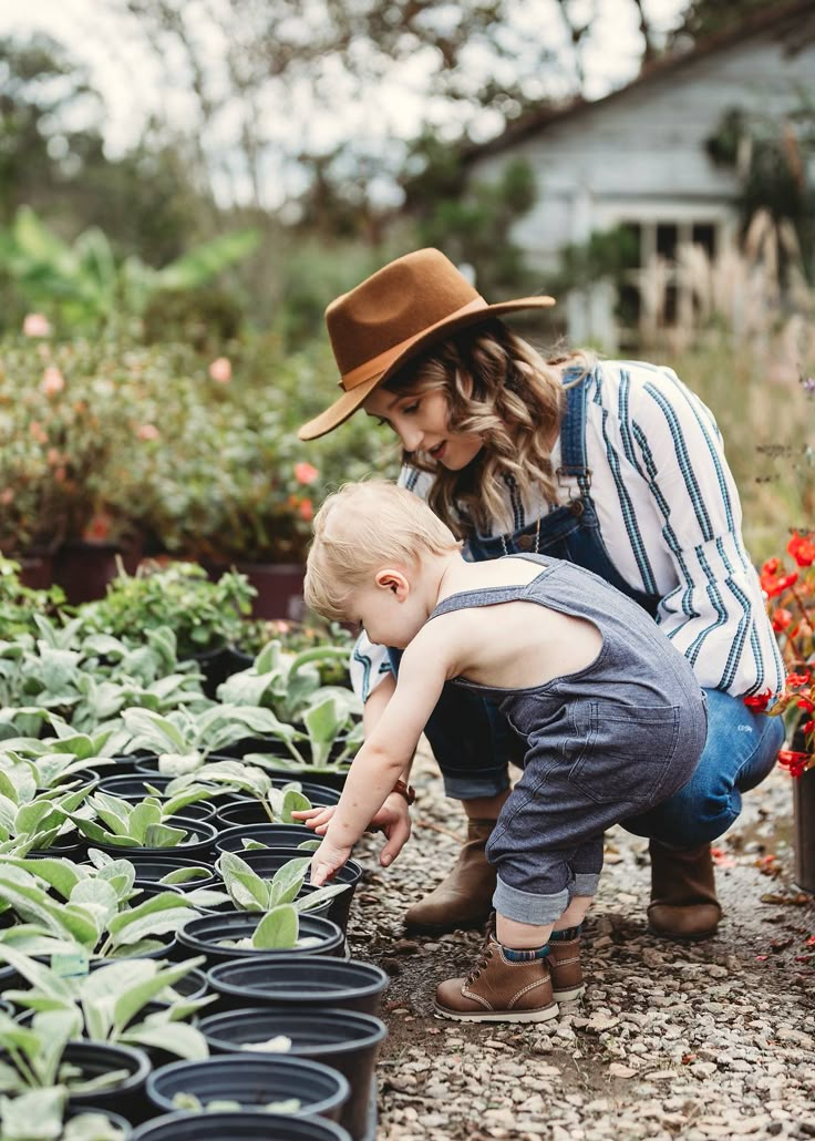 a woman and child are looking at plants in the garden together, while one boy is wearing a cowboy hat