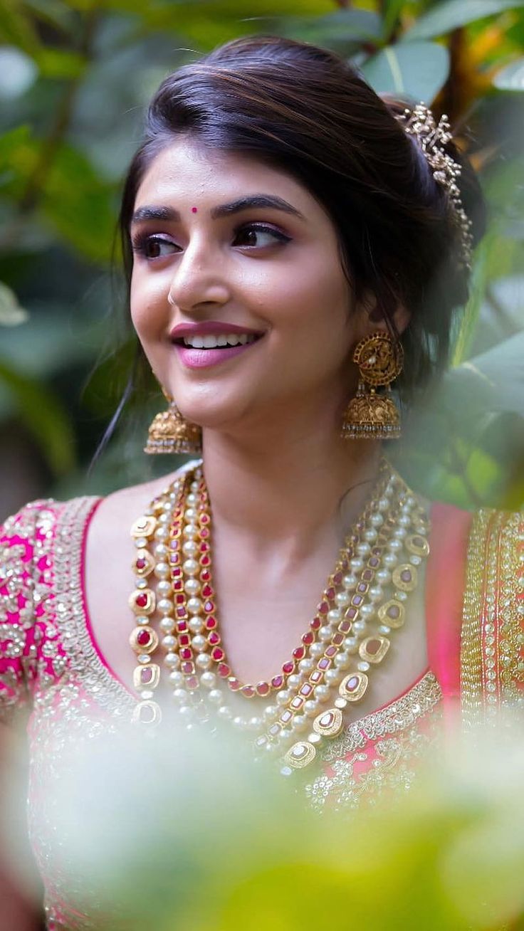 a woman in a pink and gold sari with pearls on her neck, smiling at the camera