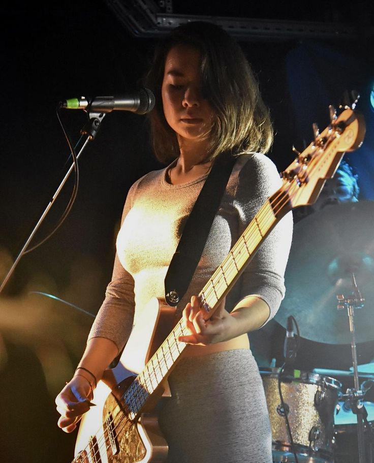 a woman holding a guitar while standing in front of a microphone