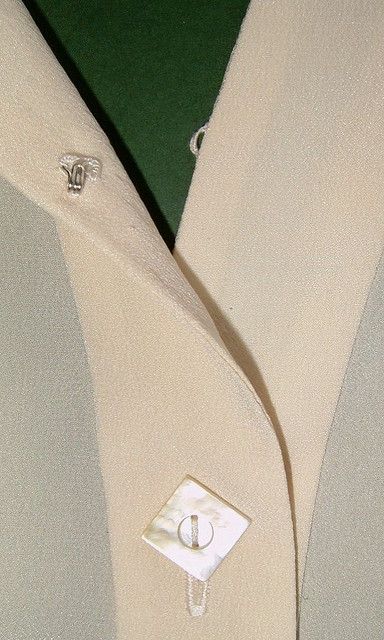 a white coat with buttons on it and a green wall in the backround