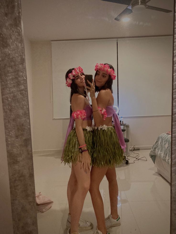 two young women in hula skirts are looking into a mirror