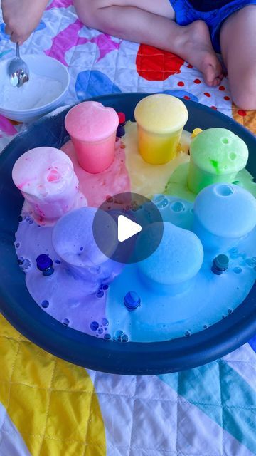 a child is playing with colored sand and water in a blue bowl on a quilt