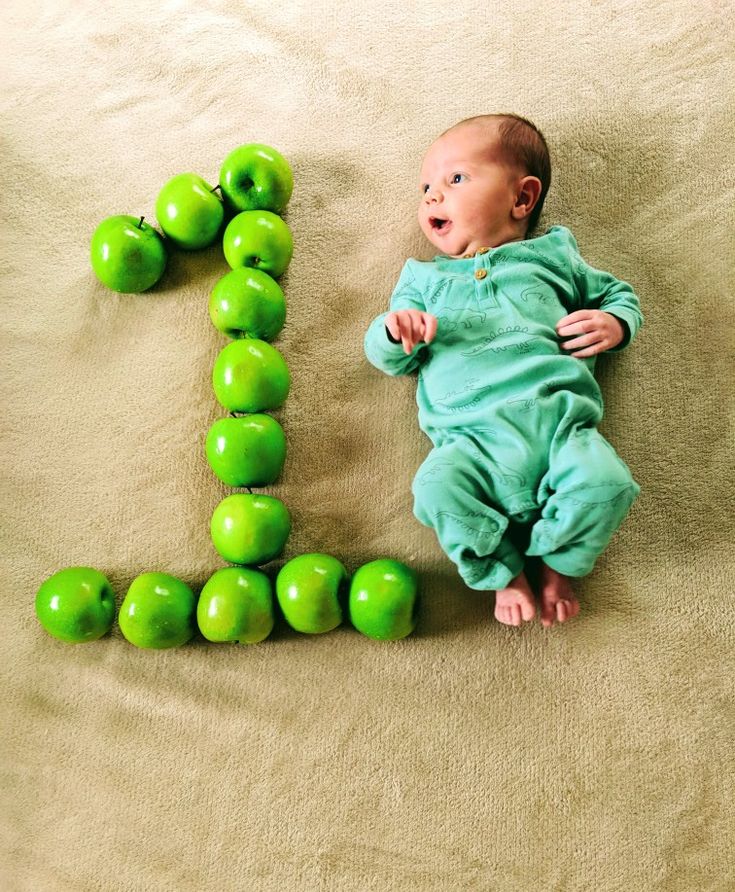 a baby laying on the ground next to green apples in the shape of the letter e