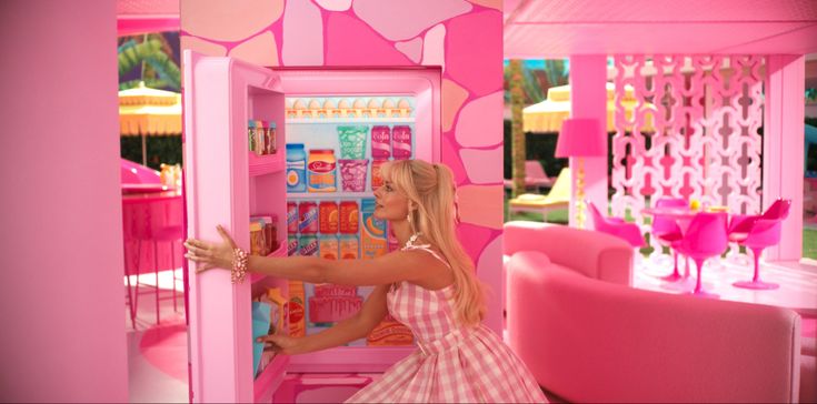 a woman in a pink dress reaching into a toy refrigerator