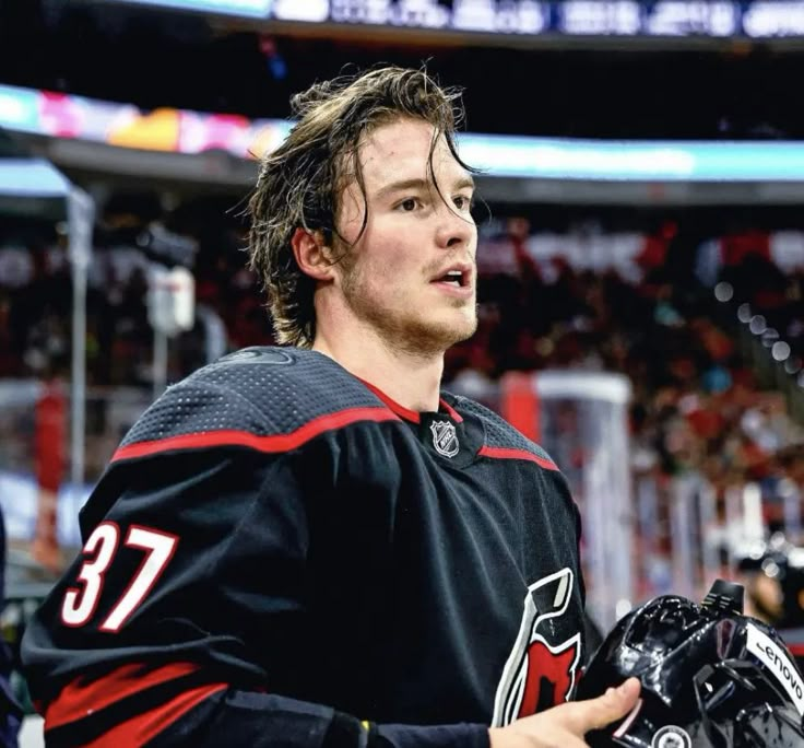 the hockey player is holding his helmet and looking off into the distance