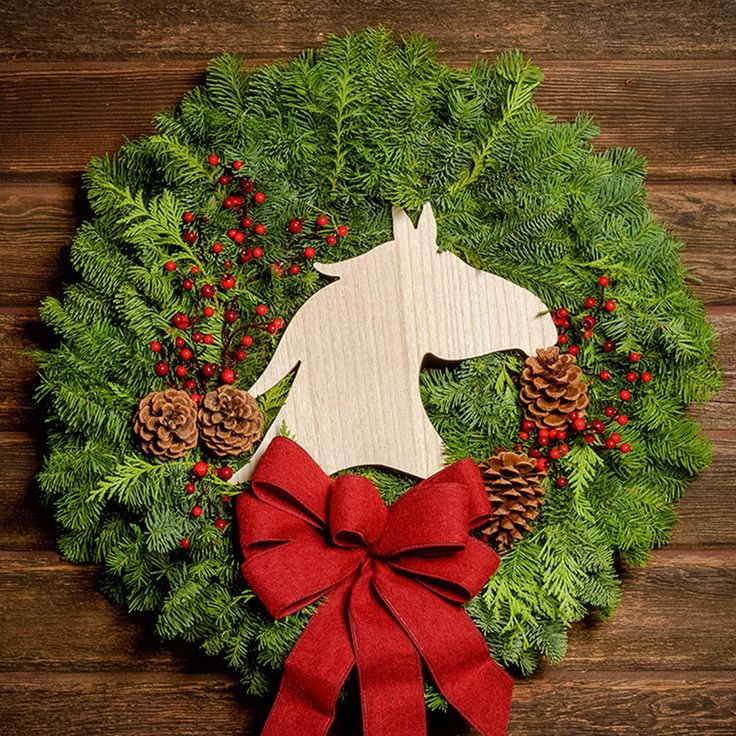 Christmas wreath made of noble fir and cedar with a wooden horse head cutout, 4 pine cones, red berry clusters, and a red brushed linen bow on a dark wood background. Cedar Boughs, Orb Lights, Horse Cutout, Horse Wreath, Horse Head Wreath, Horse Wreaths, Led Garland, Gold Hangers, Fresh Wreath