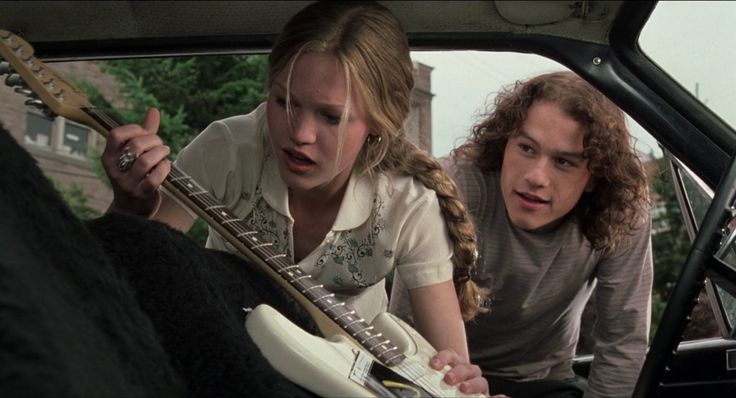 two young people are playing guitar in the back of a car while another looks on