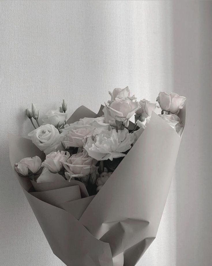 a bouquet of white roses is wrapped in gray paper and placed on the wall, ready to be delivered