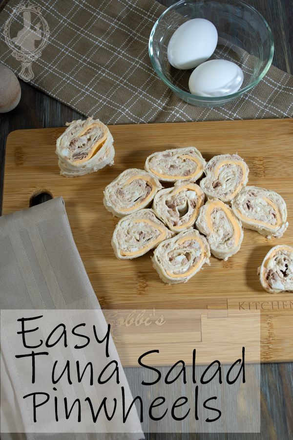 an easy tuna salad pinwheels recipe on a cutting board with eggs in the background