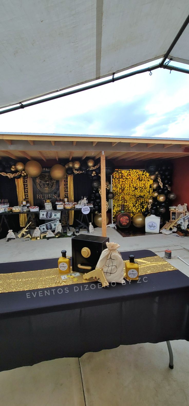 an outdoor event with black and gold decorations on the tables under a white awning