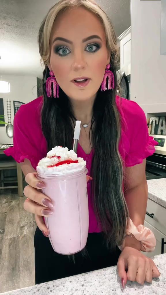 a woman with long hair holding a drink in her hand and looking at the camera