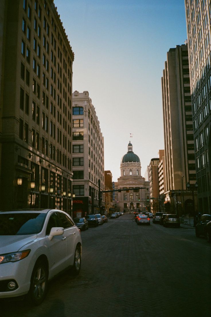 a city street with cars parked on both sides and tall buildings in the back ground