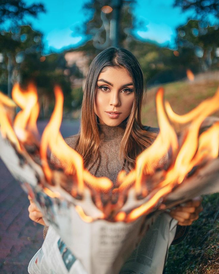 a woman with long hair is holding a newspaper in front of her face and flames around her