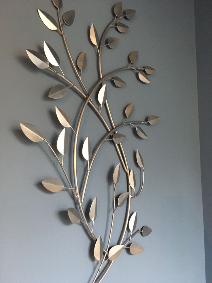 a metal wall sculpture with leaves and branches on it's side against a blue wall