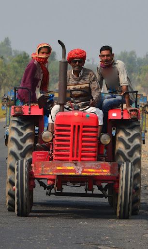 three men riding on the back of a red tractor