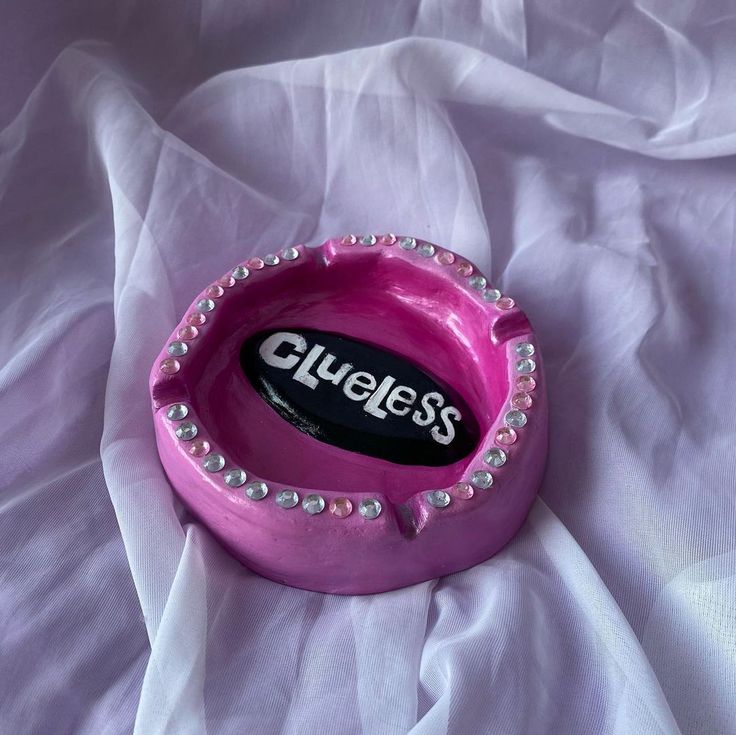 a pink bowl with the word clueless on it sitting on a white cloth covered bed