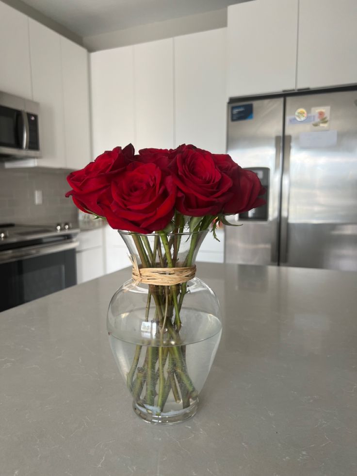 red roses are in a clear vase on the kitchen countertop with stainless steel appliances