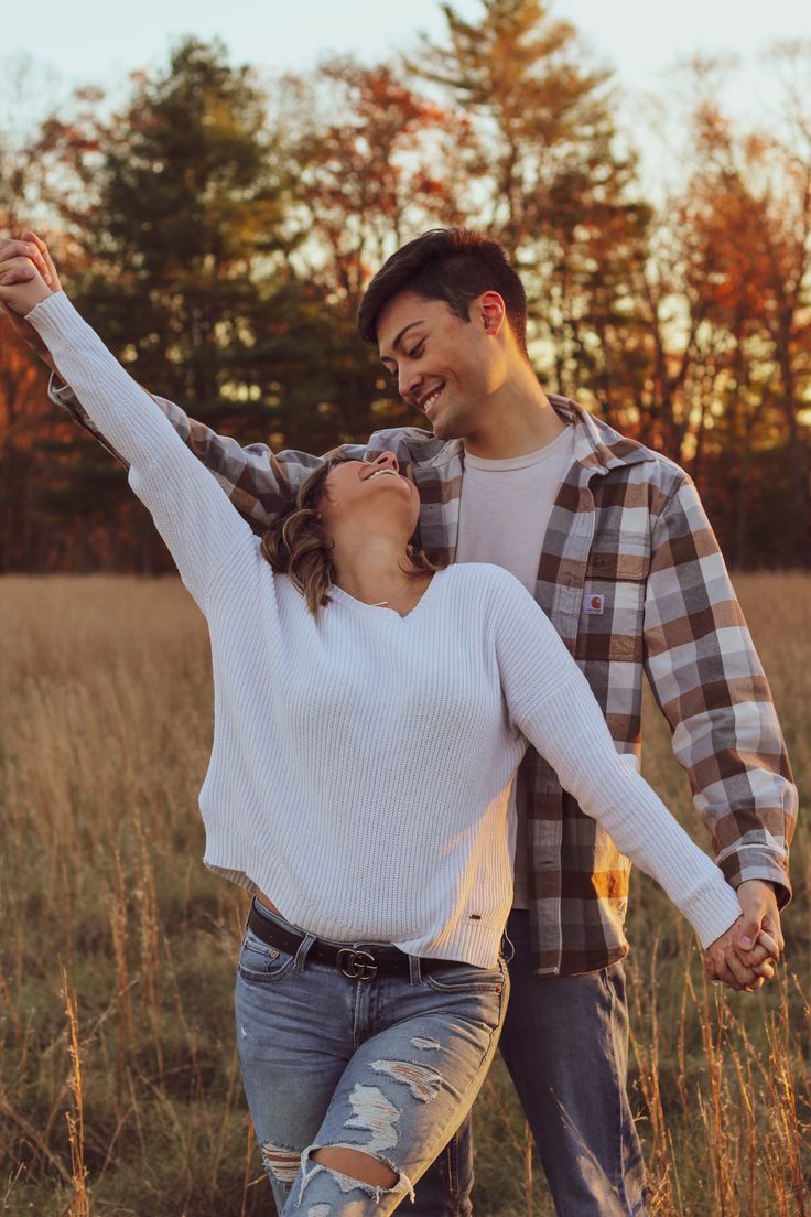 a young man and woman are dancing in the field at sunset with their arms around each other