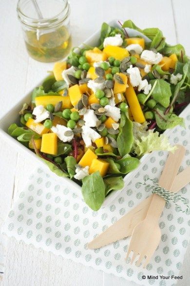 a salad in a white bowl with wooden utensils next to it on a table