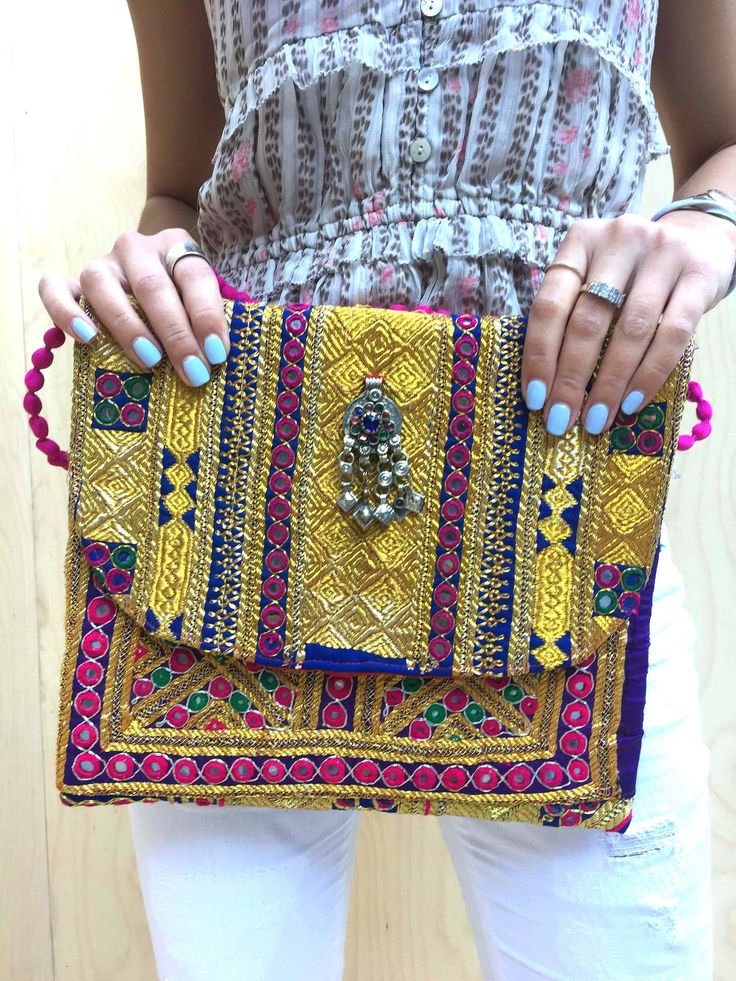 Our new bold embellished clutches come in new statement square shape and are beautiful handmade by local artisans of the Banjara tribe in India. Embellished with bold metallic thread these bags are a stunning accessory to any outfit. All bags are hand-crafted using patchworks of vintage Banjara embroidery and embellishments. According to some authorities, the Banjara lineage goes back some 2000 years. Wear as an over-sized clutch or on your shoulder with the light-weight cotton pompom chain.  Be Festive Multicolor Rectangular Shoulder Bag, Bohemian Pouch Clutch For Festive Occasions, Handmade Multicolor Rectangular Clutch, Bohemian Embroidered Rectangular Clutch, Handmade Bohemian Clutch For Festive Occasions, Festive Handmade Rectangular Shoulder Bag, Festive Bohemian Handmade Clutch, Bohemian Pouch Clutch With Multicolor Embroidery, Bohemian Multicolor Embroidered Pouch Clutch