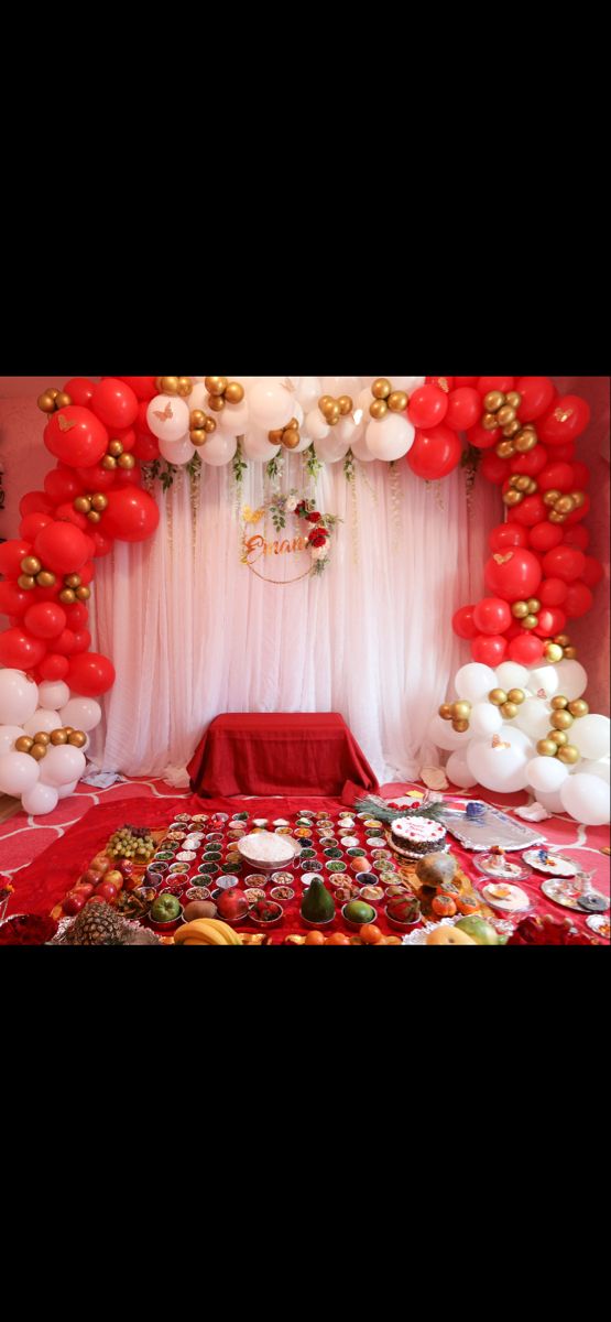 a red table topped with lots of balloons and plates covered in confetti next to a white curtain