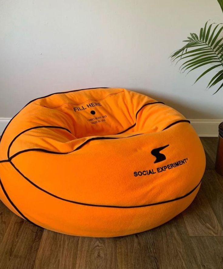 an orange bean bag chair sitting on top of a wooden floor next to a potted plant