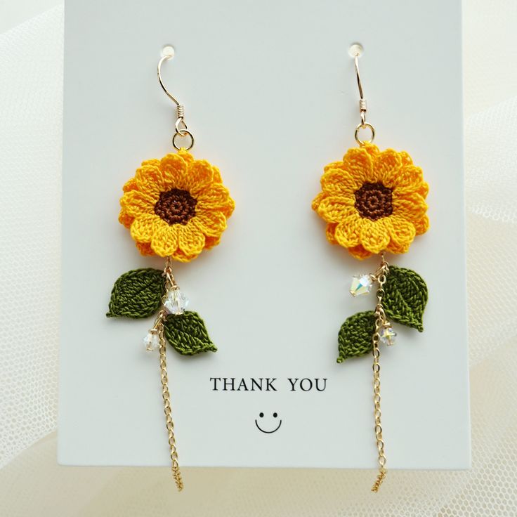 a pair of sunflower earrings with chains hanging from it's ear ends, on top of a card that says thank you