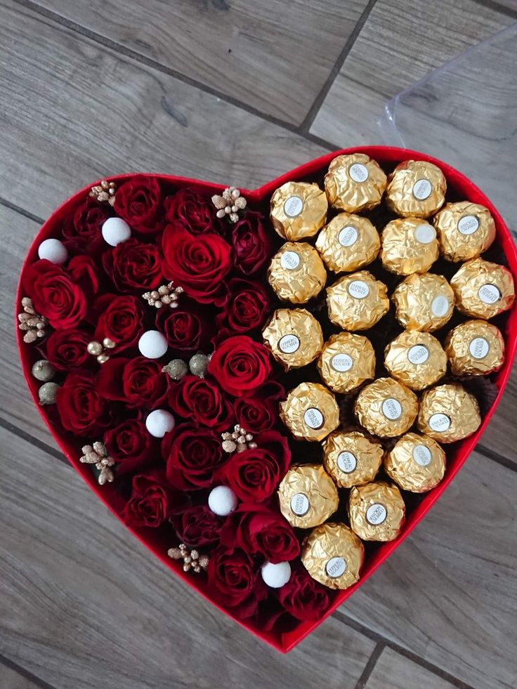 a heart shaped box filled with chocolates and roses on top of a wooden floor