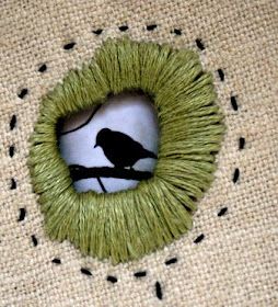 a bird sitting on top of a green piece of yarn next to a hole in the burlap