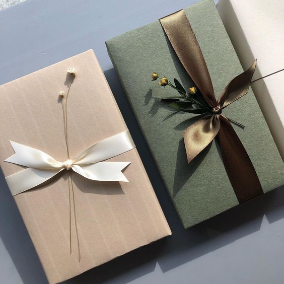 two wrapped gift boxes with ribbons and flowers on them, one is green and the other is white