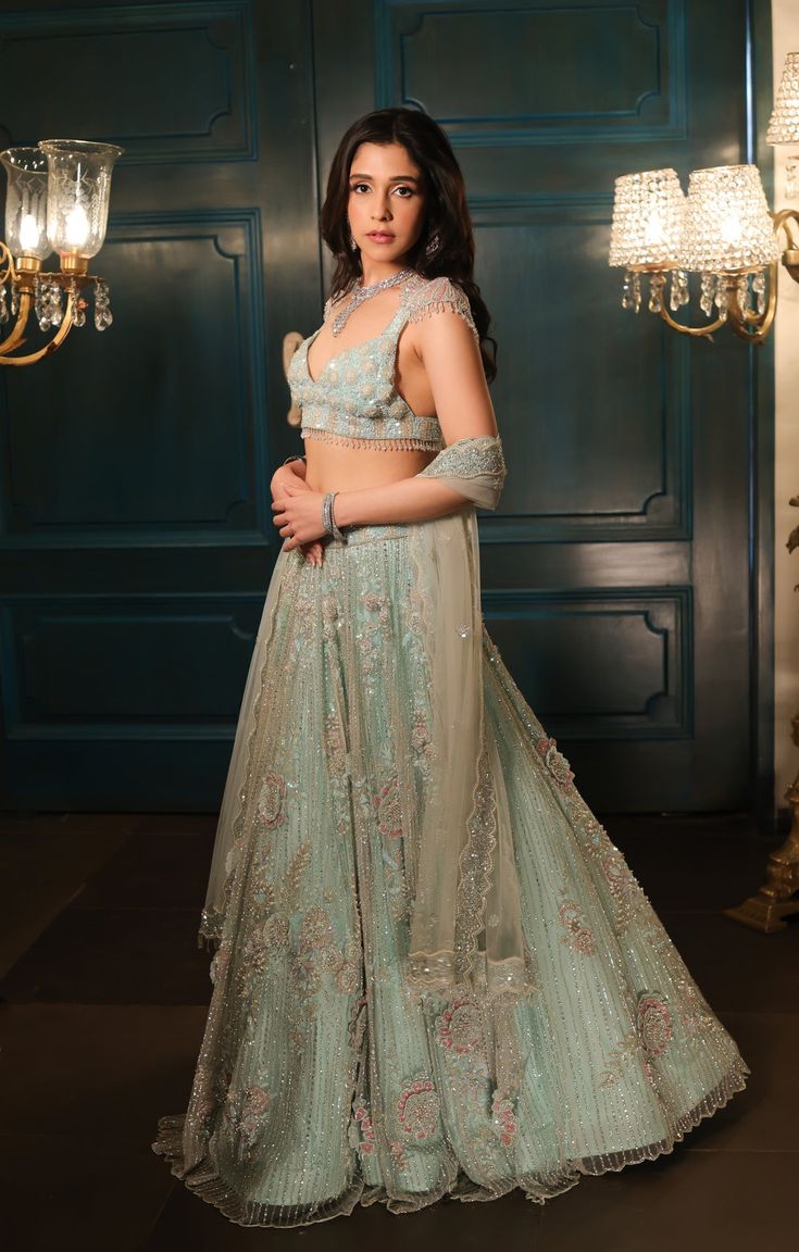 This sea green lehenga features hand embroidered 3D flowers throughout along with sequin,crystal, pearl and cutdana embroidery. It is paired with a matching V neck blouse with tassel and shoulder cap detailing, including an embroidered dupatta.From Isa by Dolly Wahal's Fiori collection.DELIVERY TIMEPlease allow 8-12 weeks for your outfit to arrive.FABRIC DETAILSNetProfessional cleaning only. Embellished Anarkali Sets In Pista Green, Green Embellished Anarkali Lehenga, Designer Embellished Green Lehenga, Green Anarkali Embellished Lehenga, Green Anarkali Style Embellished Lehenga, Festive Green Hand Embellished Sets, Green Embellished Traditional Wear For Reception, Embellished Green Traditional Wear For Reception, Embellished Green Lehenga With Traditional Drape