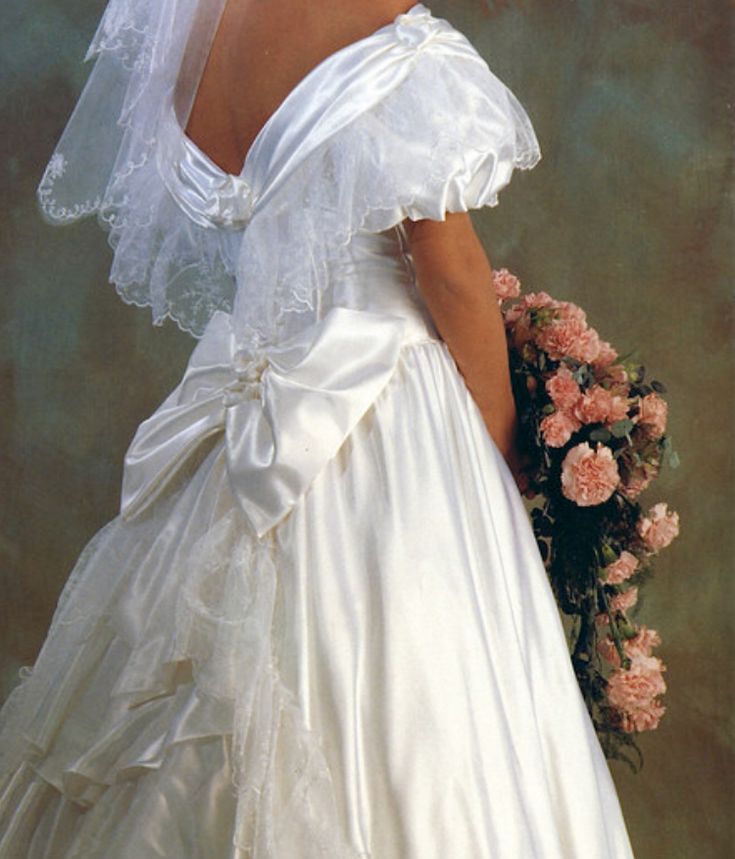 a woman in a white wedding dress holding a bouquet of flowers and wearing a veil