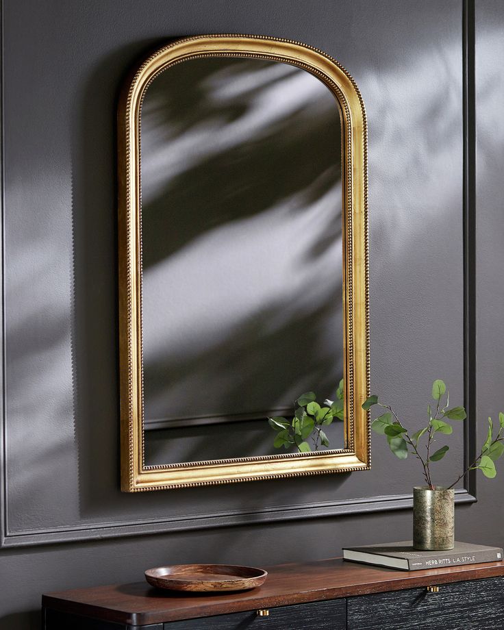 a gold framed mirror sitting on top of a wooden table next to a vase with a plant